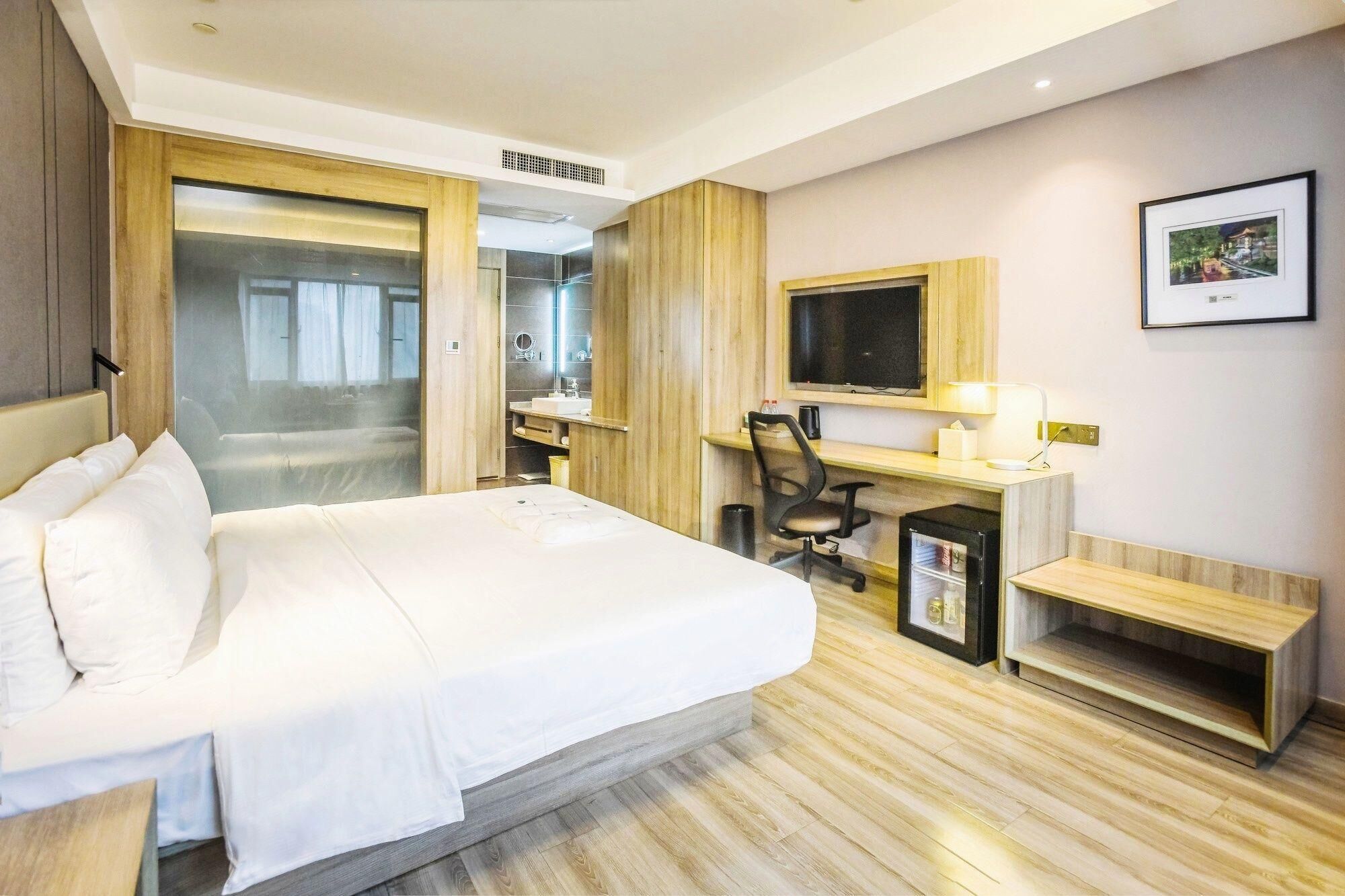 Een hotelkamer met een bed, bureau, stoel, televisie en een lijst op de muur.