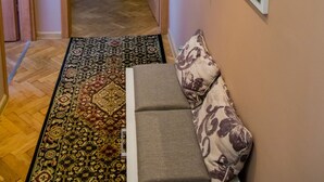 Un couloir avec un tapis à motifs, un canapé avec des coussins à motifs et une plante.