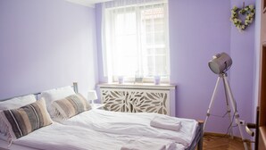 Une chambre à coucher avec un lit, une fenêtre avec des rideaux, une table de chevet et une lampe sur pied.