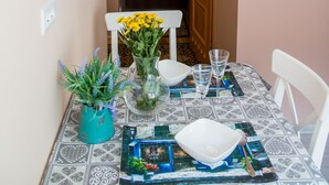 Un coin repas avec une table dressée pour deux personnes, un vase rempli de fleurs et un chemin de table décoratif.