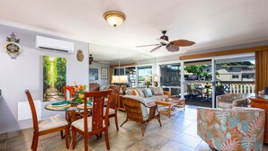 Ein geräumiges Wohnzimmer mit Essbereich, großen Fenstern, Deckenventilatoren und Blick ins Freie.