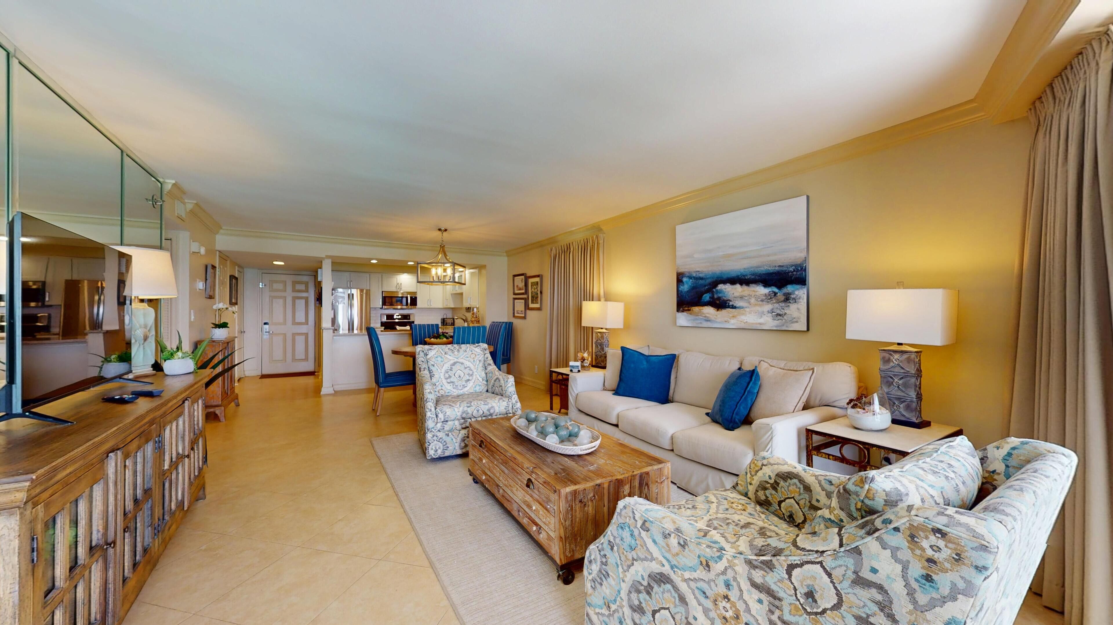 A spacious living area with a sofa, coffee table, and a dining table. There is a kitchen in the background with modern appliances.