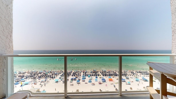 A balcony with a view of a crowded beach and the sea.