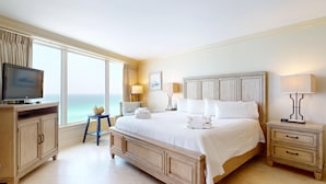 A hotel room with a large bed, a TV, a small table, and a view of the ocean.