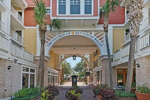 Stroll through the charming arched gateway of The Village of Baytown Wharf, surrounded by palm trees and residential-style architecture.