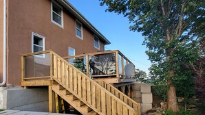 A wooden staircase leading to a balcony with a satellite dish, a tree, and a building in the background.