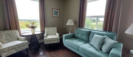 A living room with a light blue sofa, two patterned armchairs, a small table with a vase of flowers, and a lamp.