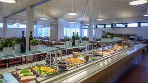 Un espace buffet comprenant différents stands de nourriture, des plantes en pot et un aménagement spacieux bénéficiant d’un éclairage naturel.