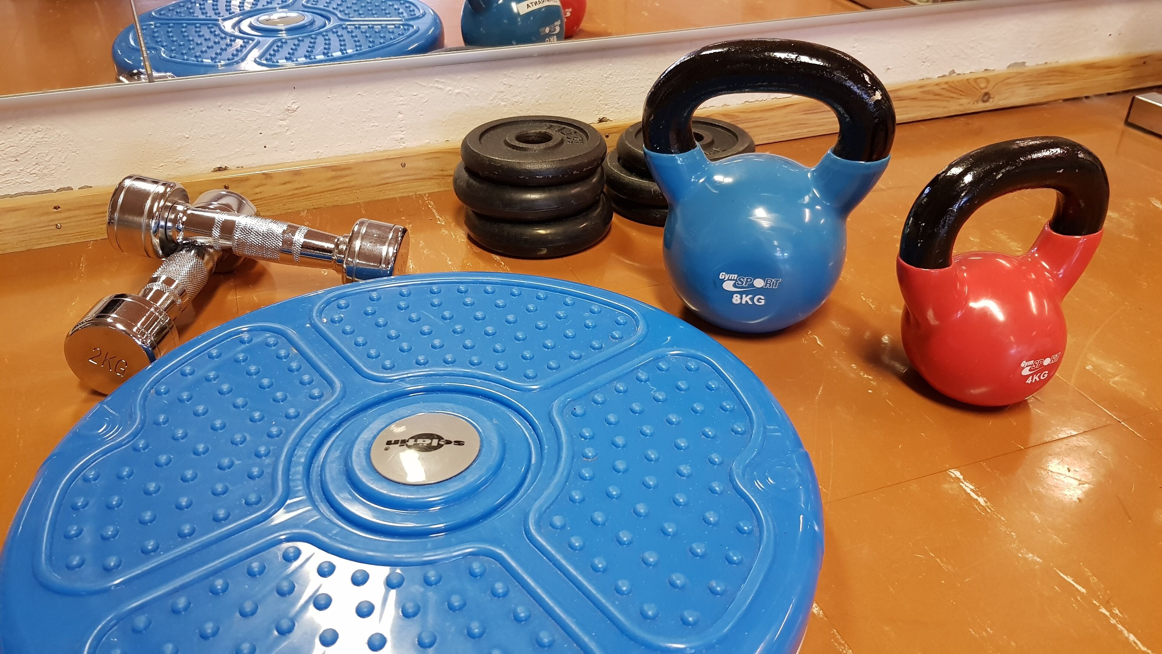 Un kettlebell bleu, un kettlebell rouge, une poignée de kettlebell bleue et un disque de poids bleu sur un plancher en bois.