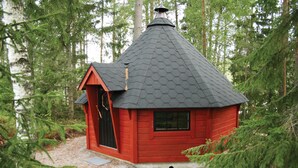 Une petite cabane en bois rouge, surmontée d’un toit conique, entourée d’arbres.