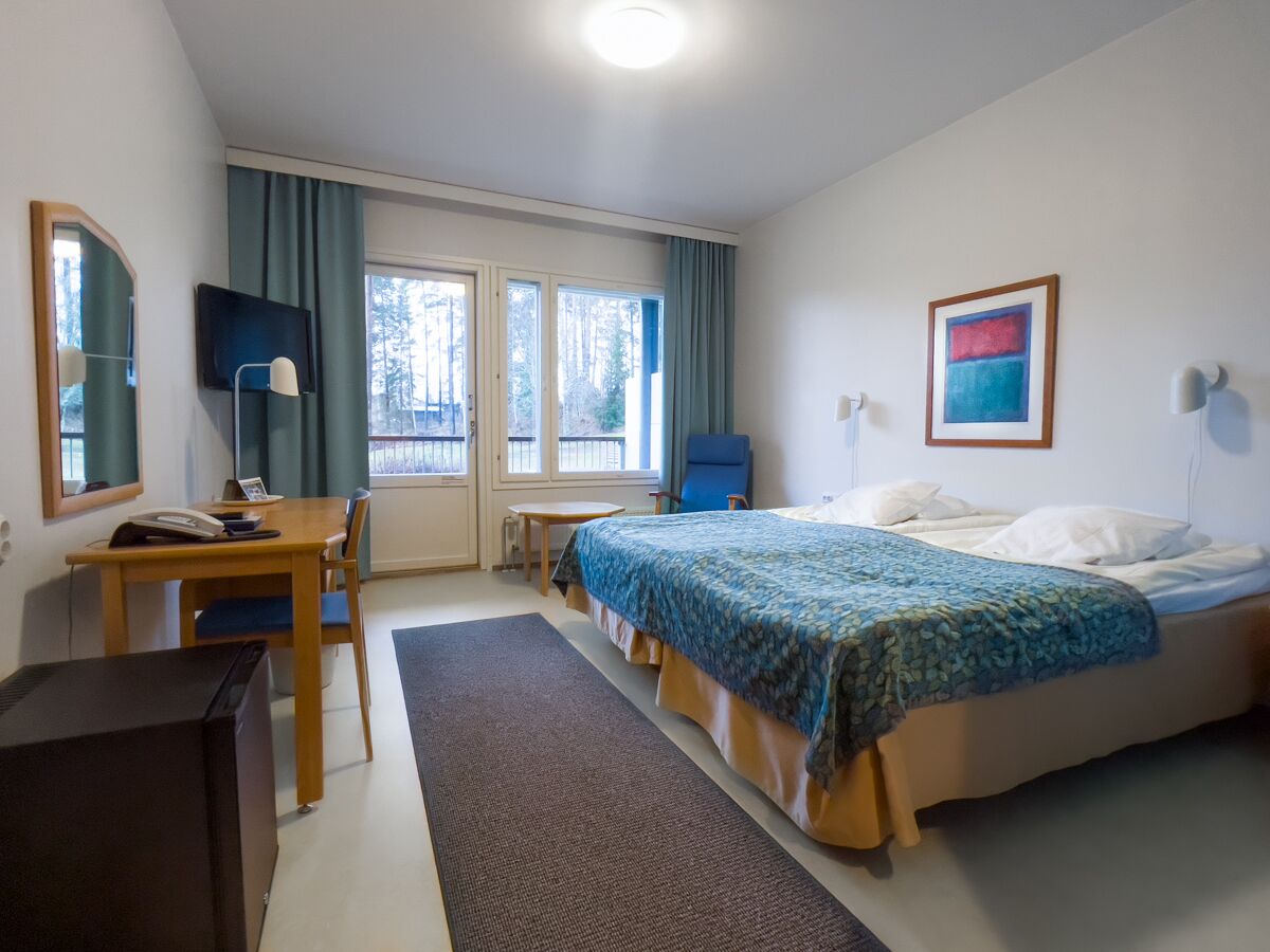 Quarto de hotel com cama, escrivaninha, cadeira e televisão.