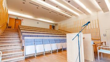 Um auditório moderno com assentos em níveis, piso de madeira e palco com um pedestal para microfone.
