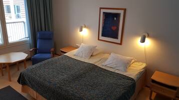 Hotellihuone, jossa on sänky, tuoli, pöytä ja ikkuna, jossa on verhot.
