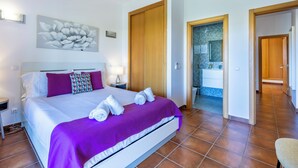Habitación de hotel moderna con una cama grande, baño con ducha de vidrio y vista al pasillo.