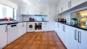 Una cocina moderna con armarios blancos, lavavajillas, horno y pileta.
