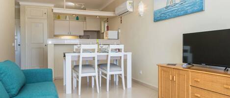 A compact living space with a dining area, kitchenette, and a television on a wooden cabinet.