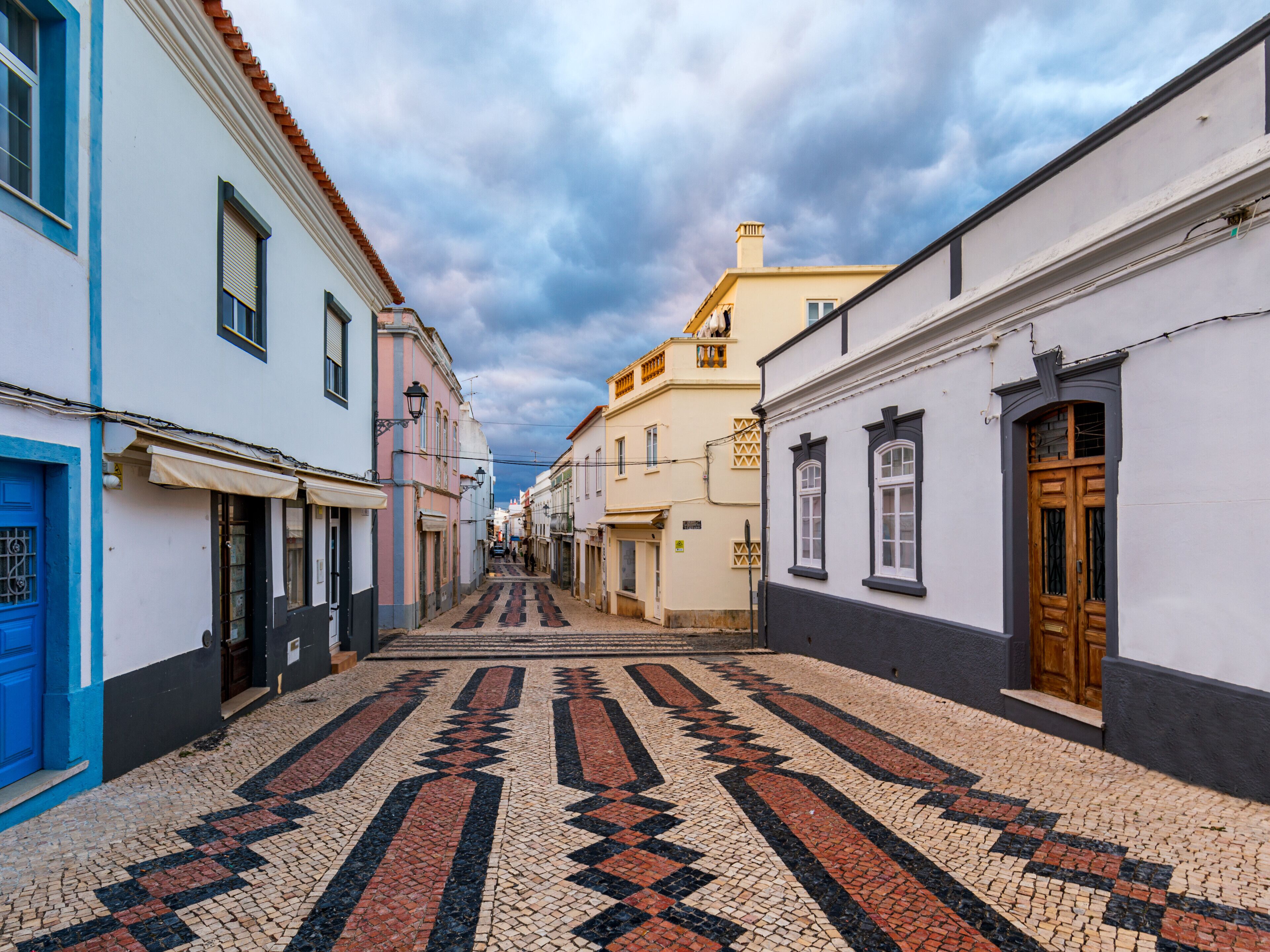 A narrow cobblestone street lined with buildings featuring traditional architecture and a patterned tile floor.