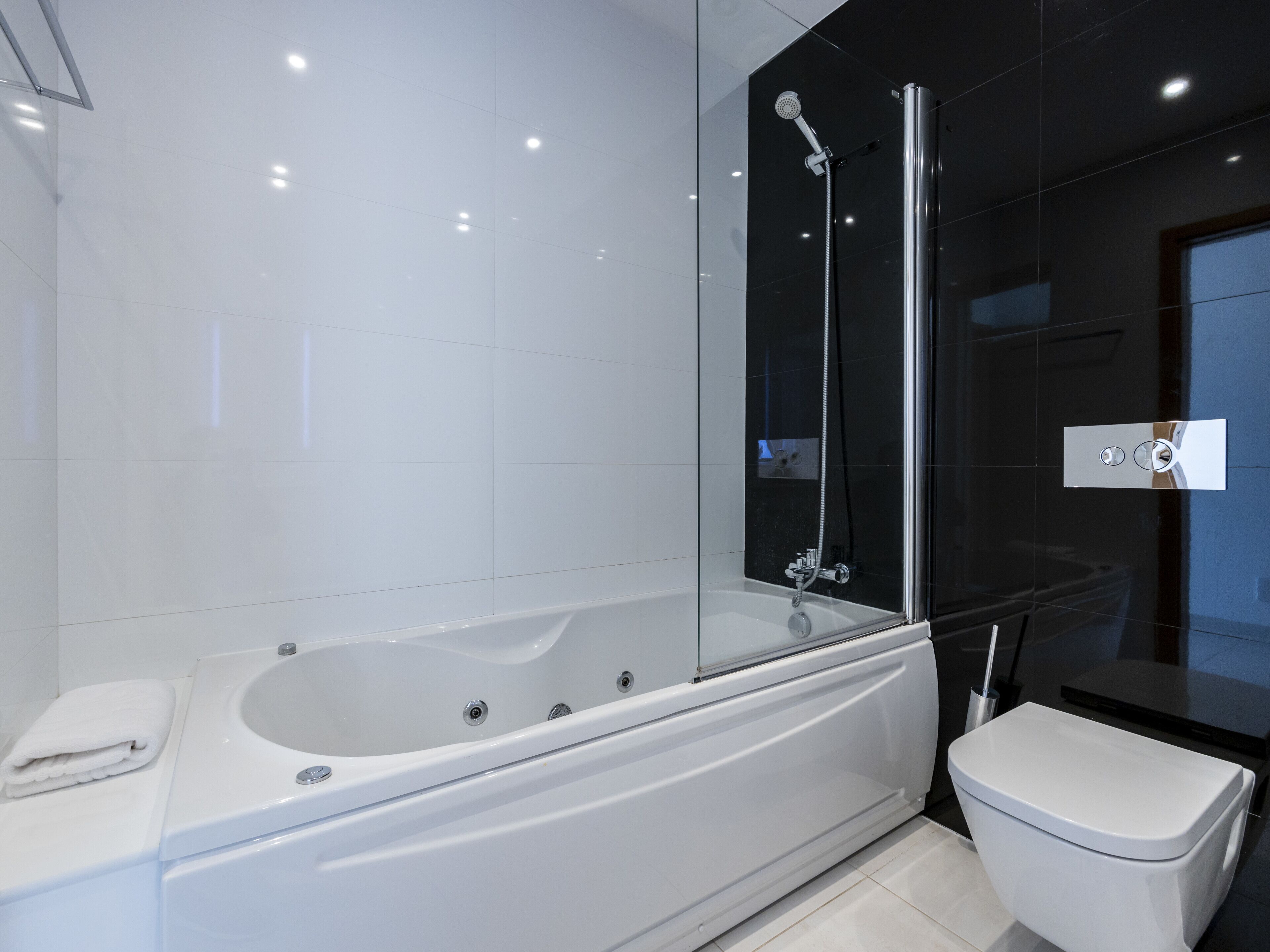 A modern bathroom with a glass-enclosed shower, a white bathtub, and a toilet.