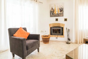 Relax in this inviting living room with a cozy armchair, fireplace, and beautiful sailboat painting.