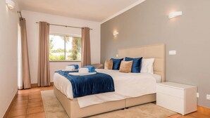 Une chambre à coucher avec un lit, une table de chevet, une fenêtre avec des rideaux et une vue sur la verdure à l’extérieur.