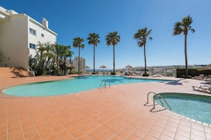 A swimming pool with a tiled deck, palm trees, and a view of the sea.