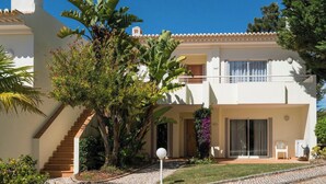 Un immeuble de deux étages avec une façade blanche, un balcon et un escalier menant à l’entrée.