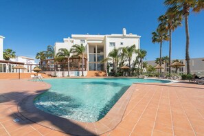 Un hotel modern amb piscina, palmeres i un cel blau clar.