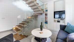A modern living room with a glass staircase, a flat-screen TV, a round coffee table, and a bookshelf. - Casa Machado Old Town Lagos (Lagos)