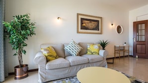 A living room with a beige sofa, a round coffee table, a potted plant, and a framed artwork on the wall. - Sunny Seaside Escape (Lagos)