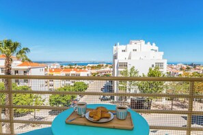 Een balkon met een ontbijttafel, met uitzicht op een kustplaats.