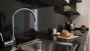 A modern kitchen with a stainless steel sink, a curved faucet, and a wooden cutting board with bread and jars. - Central Modern 2-Bed Apartment Armação De Pera (Armação de Pêra)