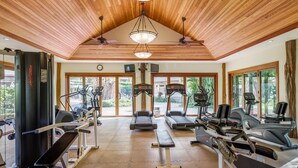 A gym with treadmills, elliptical machines, and weight equipment, featuring wooden ceilings and large windows. - Home Away From Home - Beautiful Townhome in the Heart of Mauna Lani (Kamuela)