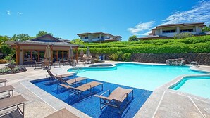 A swimming pool with lounge chairs and umbrellas, surrounded by a landscaped garden and a stone wall. - Home Away From Home - Beautiful Townhome in the Heart of Mauna Lani (Kamuela)