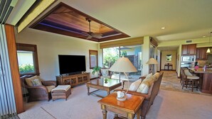 A spacious living room with a flat-screen TV, comfortable seating, a coffee table, and a dining area with a kitchen in the background. - Home Away From Home - Beautiful Townhome in the Heart of Mauna Lani (Kamuela)