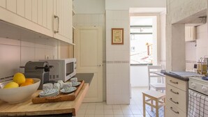 Eine kleine Küche mit weißen Schränken, einer Mikrowelle, einem Toaster und einem Holztisch mit einer Obstschale und einem Teeservice.
