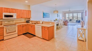 A modern kitchen with wooden cabinets, a built-in microwave, and a dishwasher. There is a dining area with a view of the city through large windows.