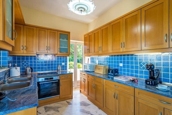 A kitchen with wooden cabinets, a blue tiled backsplash, a sink, an oven, and a countertop with a coffee maker and other appliances.