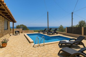 A swimming pool with lounge chairs, a stone patio, and a view of the sea.