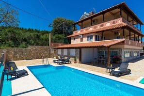 A two-story building with a swimming pool, outdoor seating, and a stone wall.