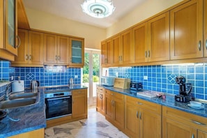 A kitchen with wooden cabinets, a blue-tiled backsplash, a built-in oven, and a coffee maker. - Panorama Sea Breeze - Pool Dream Gem (Polemarchi)
