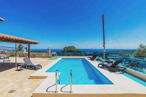 Una piscina rettangolare con due scalette in metallo, circondata da sedie a sdraio e un patio in pietra.