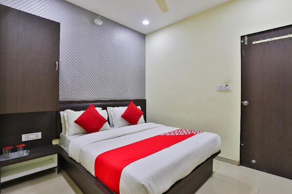 A hotel room with a bed, a nightstand, a wardrobe, and a wall with a geometric pattern.