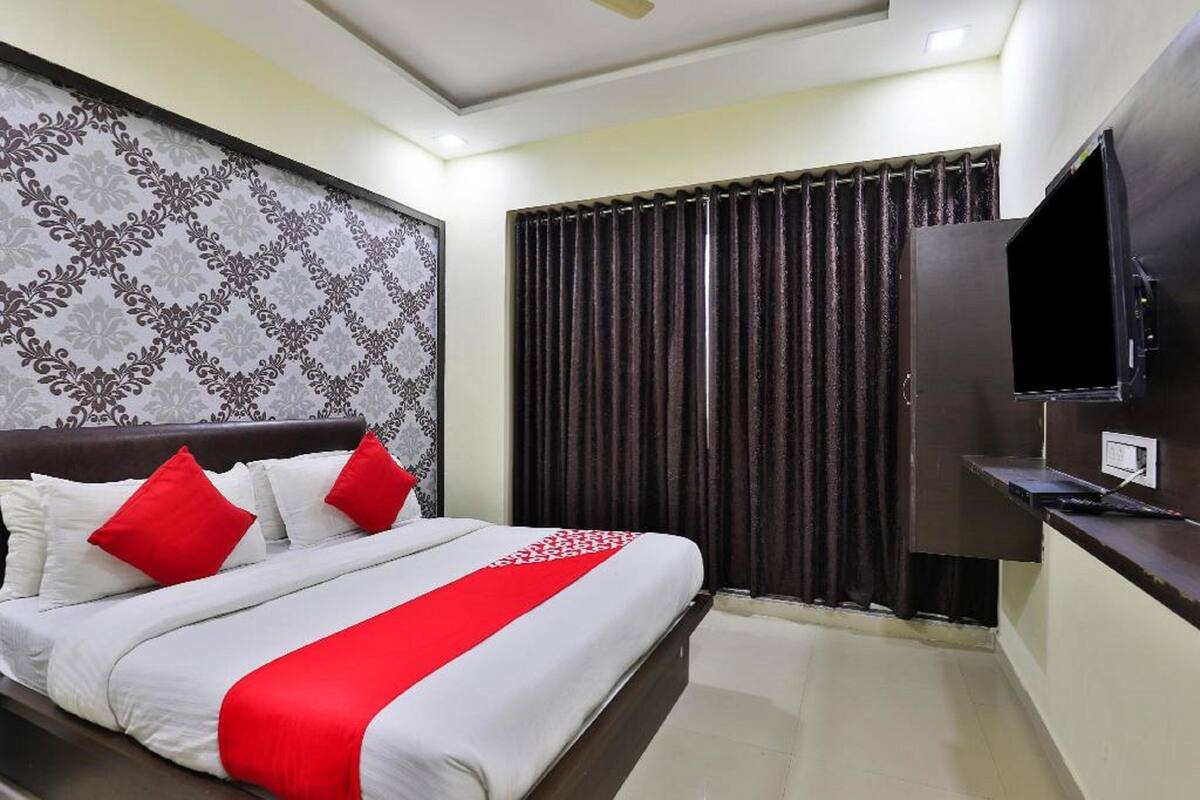 A hotel room with a large bed, a flat-screen TV, a dark-colored headboard, and a patterned wallpaper on the wall.