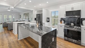 A modern kitchen with white cabinetry, a large island with a marble countertop, a stainless steel refrigerator, a built-in oven, and a gas stove. - Cozy WaterColor Condo - 3rd Floor Unit, Steps to Beach Club & Seaside, Bikes! (Santa Rosa Beach)