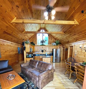 Interior de una cabaña de madera con comedor, cocina y ventilador de techo.