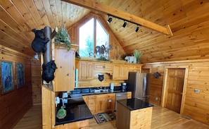 Cocina de cabaña de madera con una isla central, armarios de madera, un refrigerador de acero inoxidable y decoración con motivos de osos.
