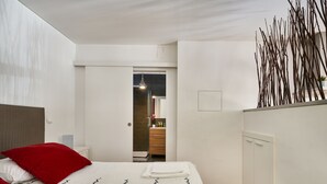 Une chambre à coucher moderne avec un grand lit, des oreillers rouges, une table de chevet et un dressing.