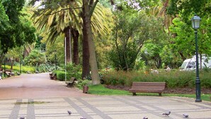 Un sentier aménagé dans un parc, avec des bancs et un panneau indiquant « HÔTEL CHELAS ».