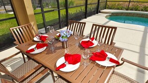 A dining table set for four with red napkins and white plates, surrounded by wicker chairs, near a pool. - Solterra Resort-4183eodjgil 6 Bedroom Home by RedAwning (Davenport)