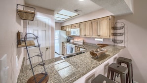 A kitchen with granite countertops, wooden cabinets, a stainless steel sink, and a microwave. - The Iron Cactus on the Comal CW C102 2 Bedroom Condo by RedAwning (New Braunfels)